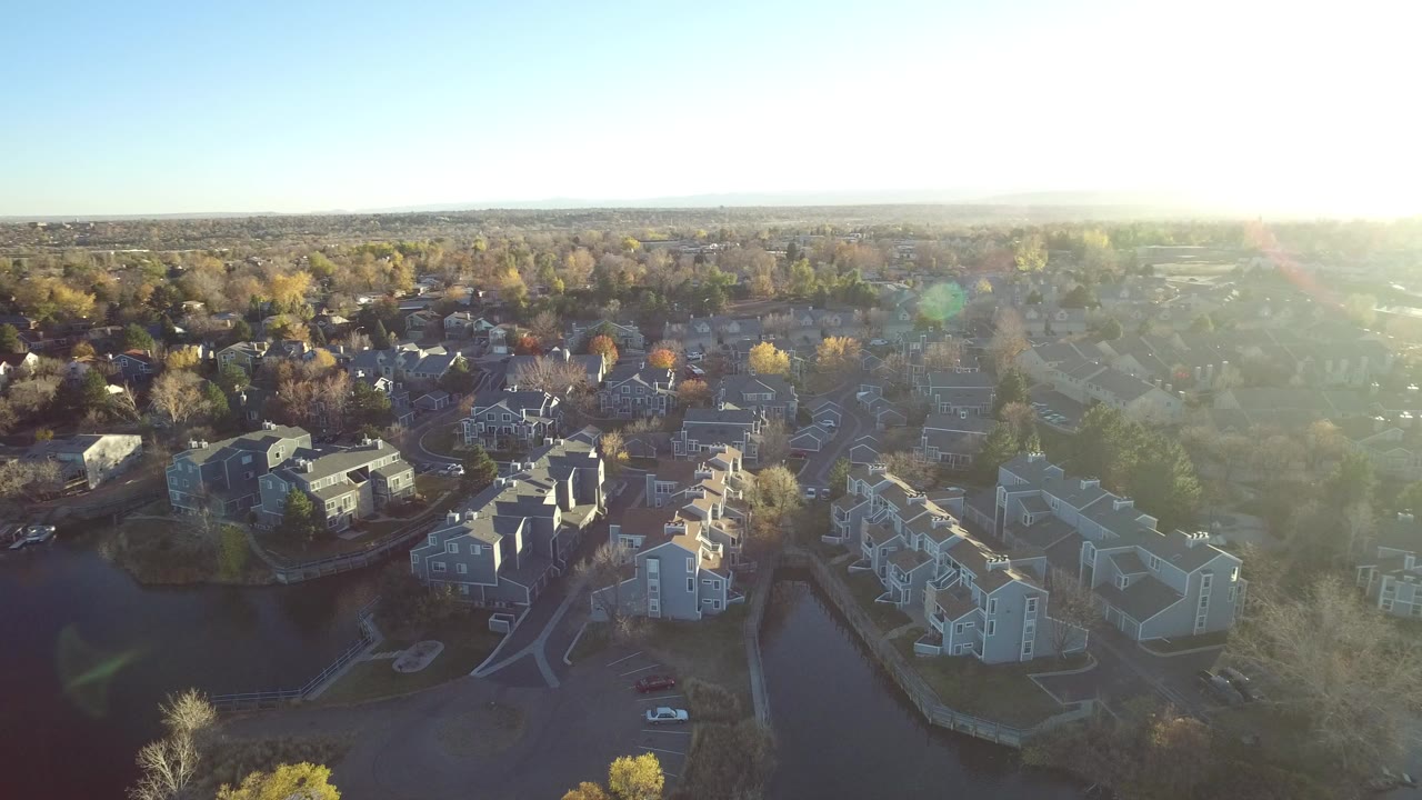 Aerial view of lakeside homes and trees under bright sun glare.