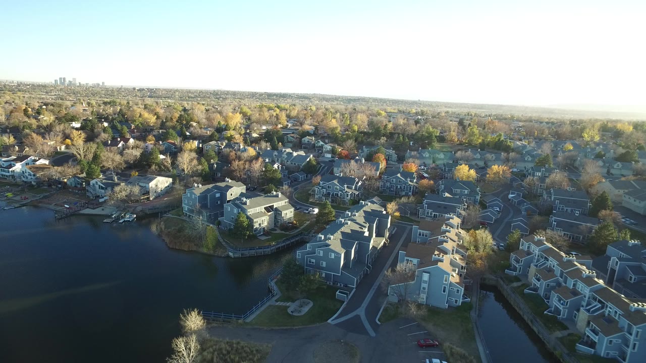 Aerial view of lakefront homes and trees under a bright sky.