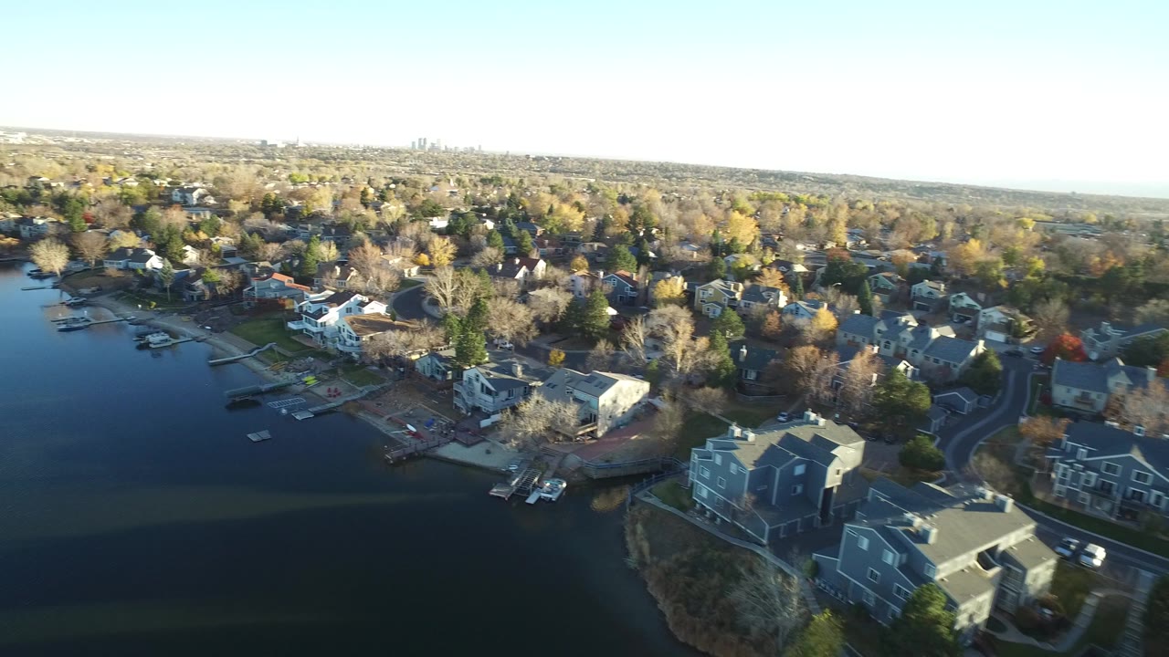 Aerial view of lakefront suburban homes and docks under clear sky.