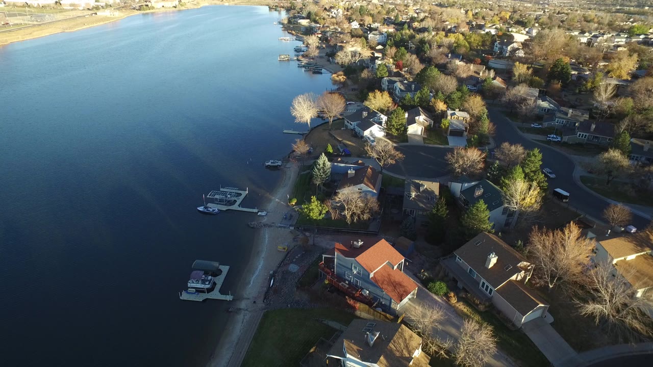 Aerial view of lakefront houses, docks, boats, roads, and trees.