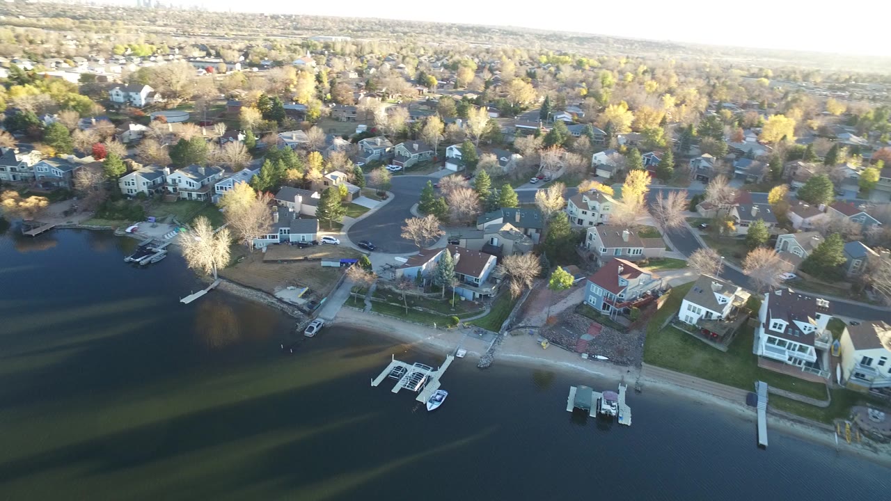 Aerial view of lakeside homes, docks, and boats beside dark water.