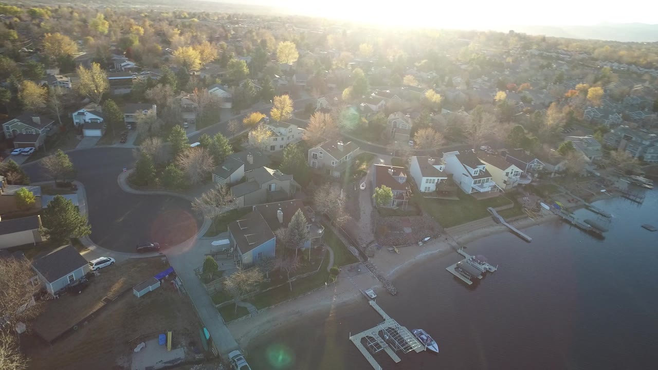Aerial view in Westminster, Colorado with a curved residential street at left, homes and docks near the shoreline, open water at right, and no visible people.