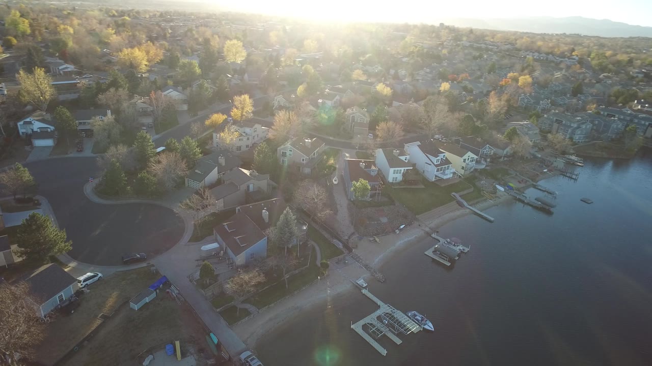 High aerial view of lakefront houses, docks, trees, and open water.
