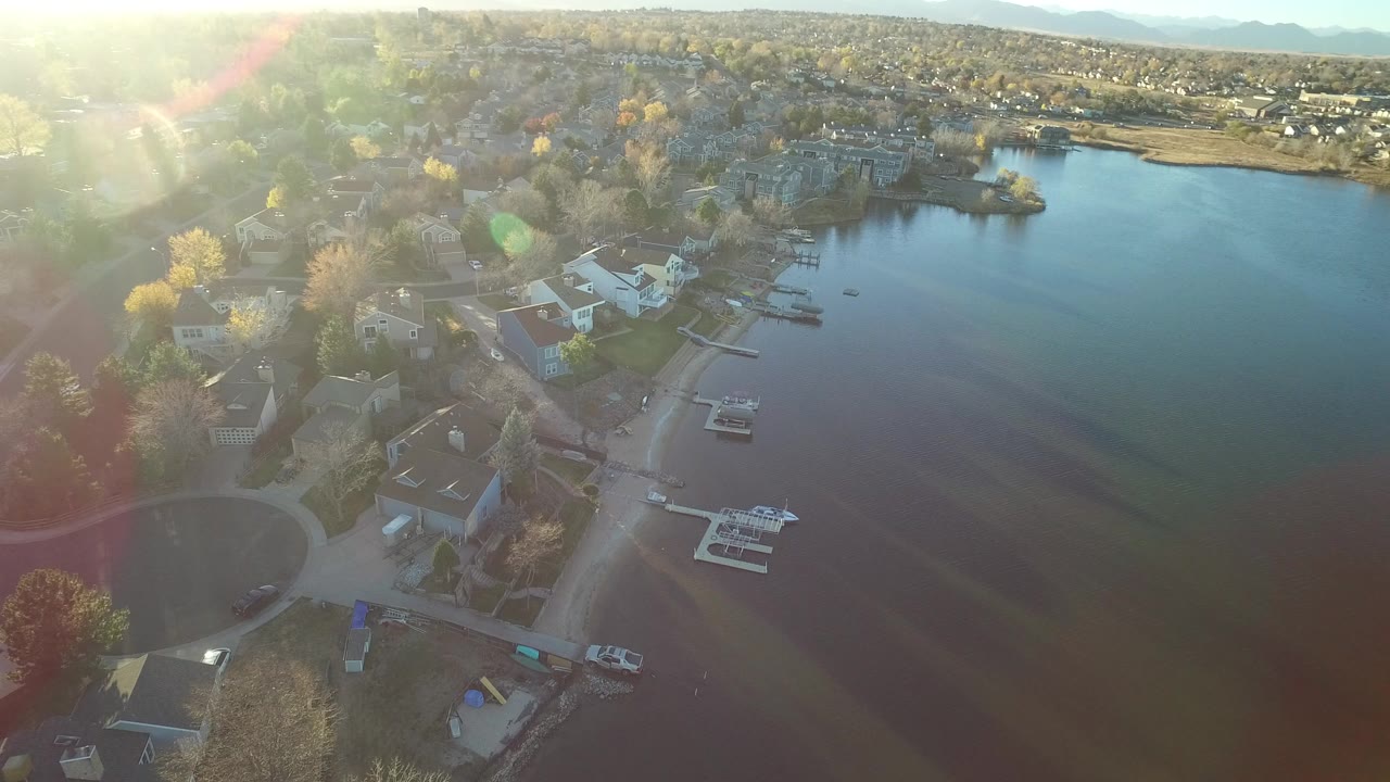 Aerial view of lakeside houses and docks beside a quiet neighborhood street.