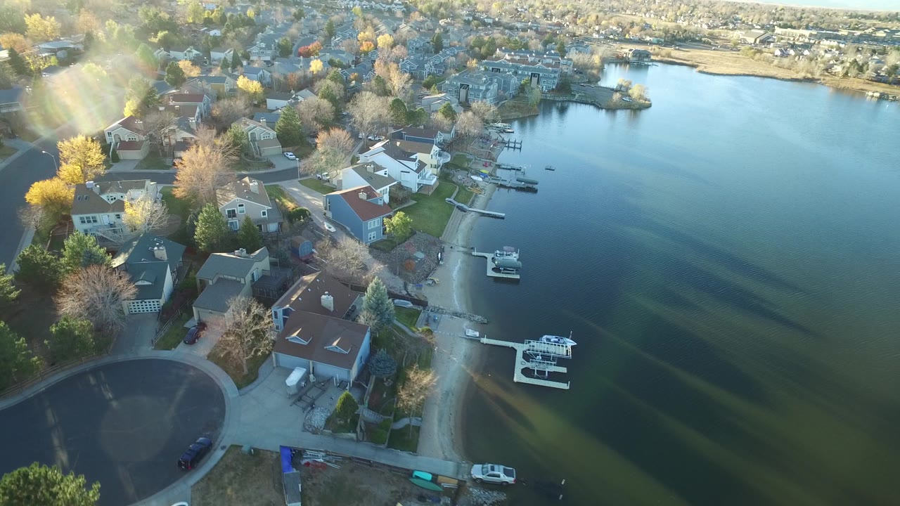 Drone-like aerial view of a residential lakeshore with docks and moored boats.
