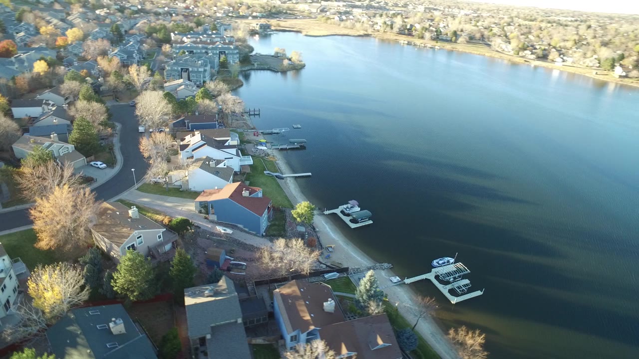Aerial view over Westminster, Colorado waterfront homes with docks and moored boats extending into the lake, with no visible people.