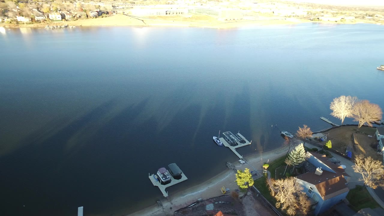 Elevated view over blue lake water in Westminster, Colorado, with residential docks, small boats, shoreline houses, and no clearly identifiable people.