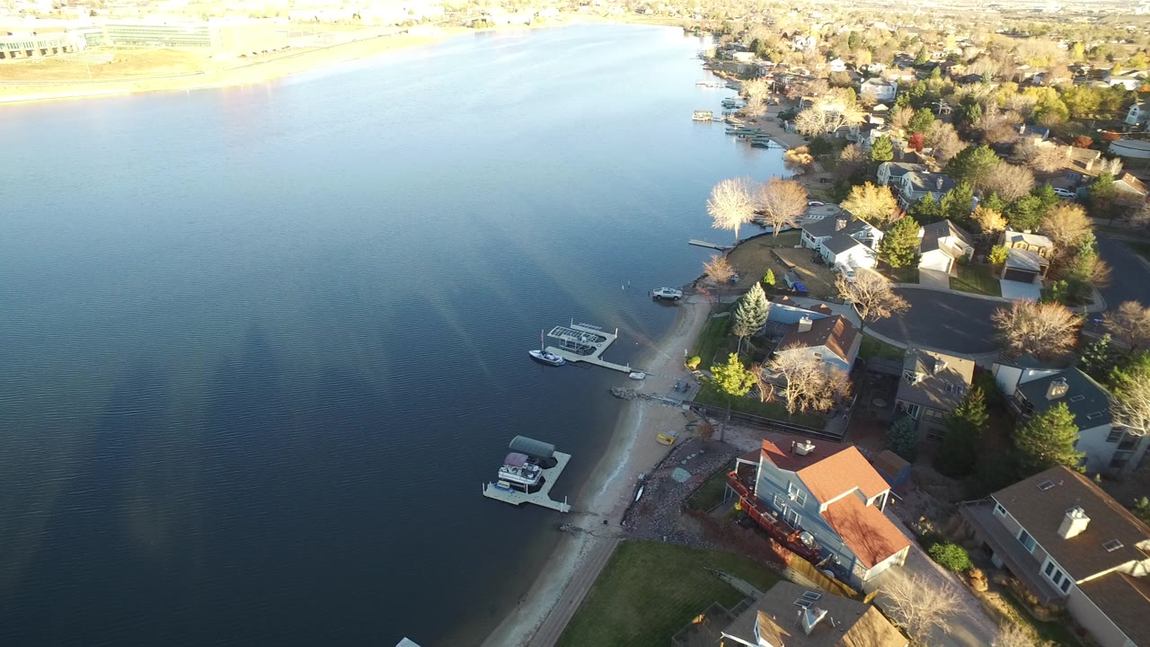Aerial view of lakefront homes, docks, and small boats beside calm water.