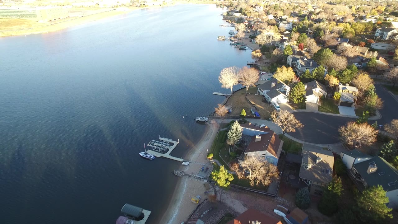 Aerial frame in Westminster, Colorado with the lake occupying most of the left side, shoreline houses and docks on the right, and no visible people.