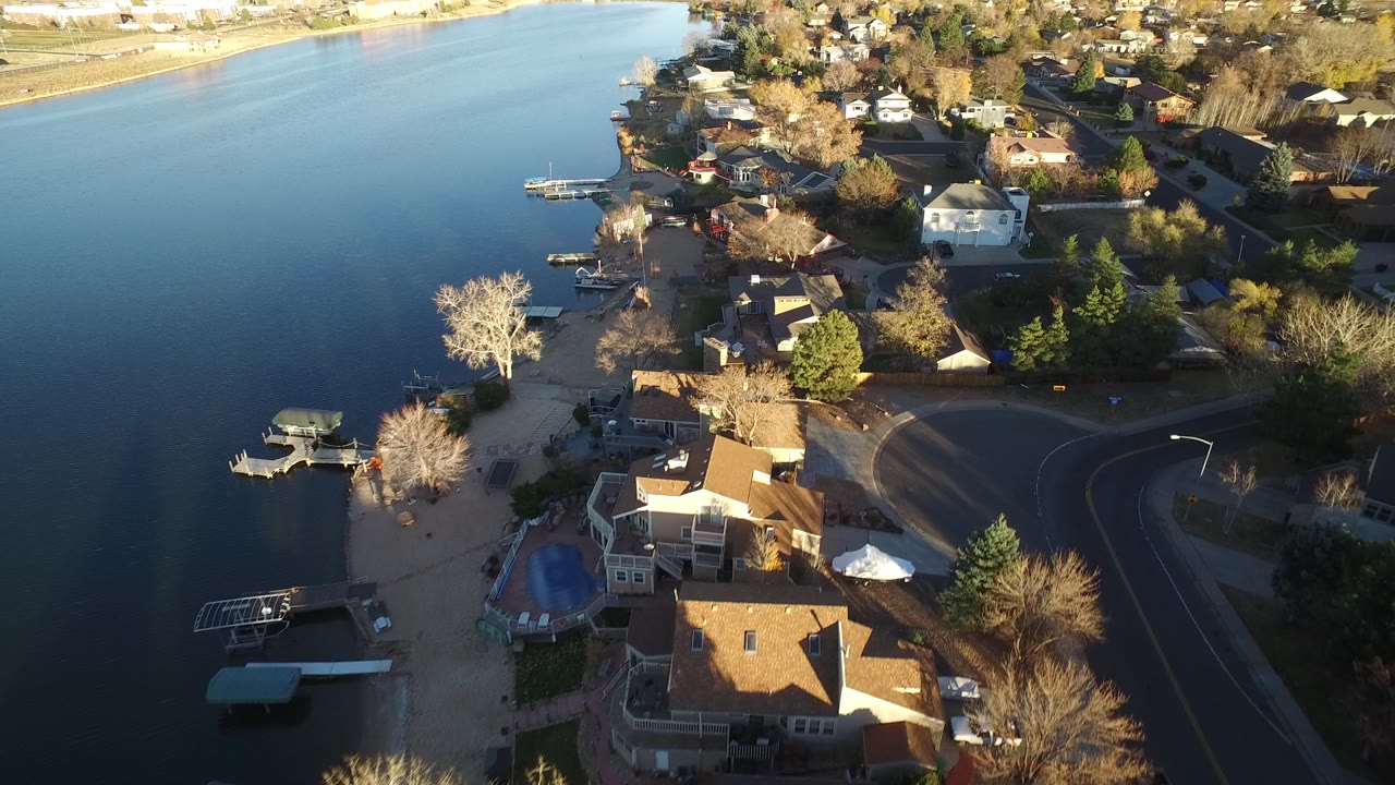 Aerial neighborhood view with water, docks, roofs, and road.