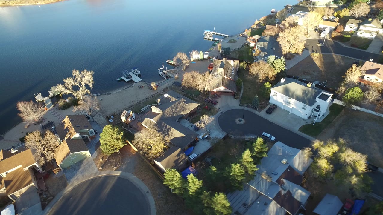 Aerial view of lakefront homes, trees, docks, and a curved residential street.