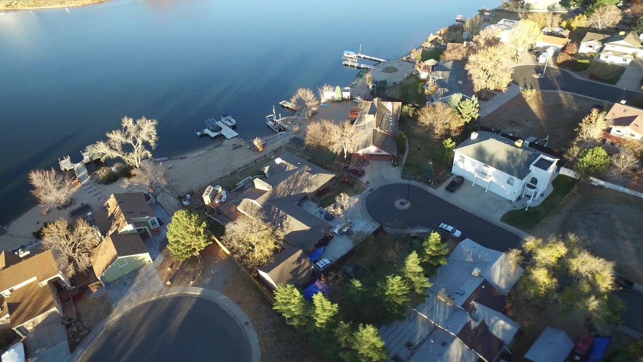 Westminster, Colorado aerial view with lake water across the top of frame, clustered homes and yards below, shoreline docks, and no visible people.
