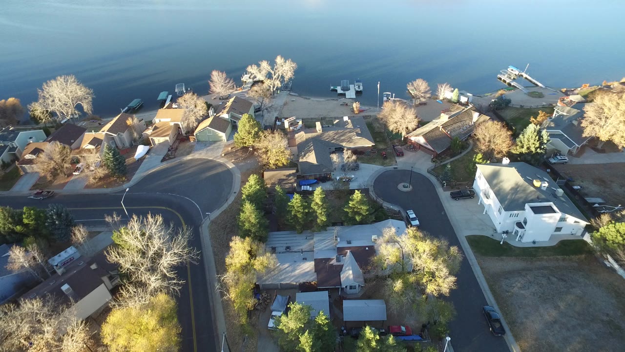 Overhead view of lakefront homes, a curved street, trees, and parked cars.