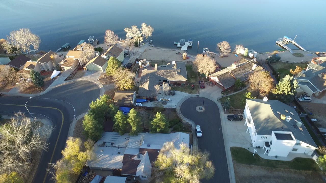 Aerial view of waterfront homes beside calm water and curved residential roads.