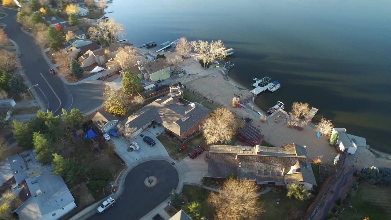 Aerial view of lakeside homes, docks, boats, and a curved street beside dark water.