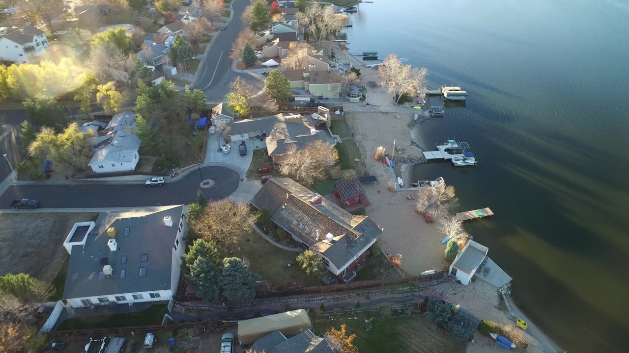 Aerial view of lakeside homes, a curved street, docks, boats, and water.
