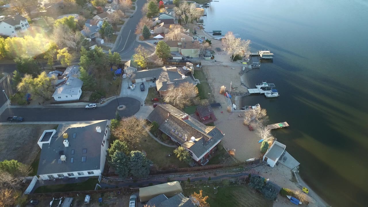 Aerial view in Westminster, Colorado showing waterfront houses, a cul-de-sac-like curve in the road, small docks, moored boats, trees, and no visible people.