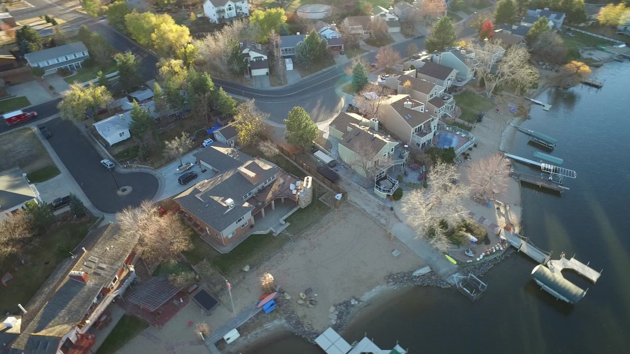 Aerial view of lakeside homes, docks, sandy shore, and curving roads.