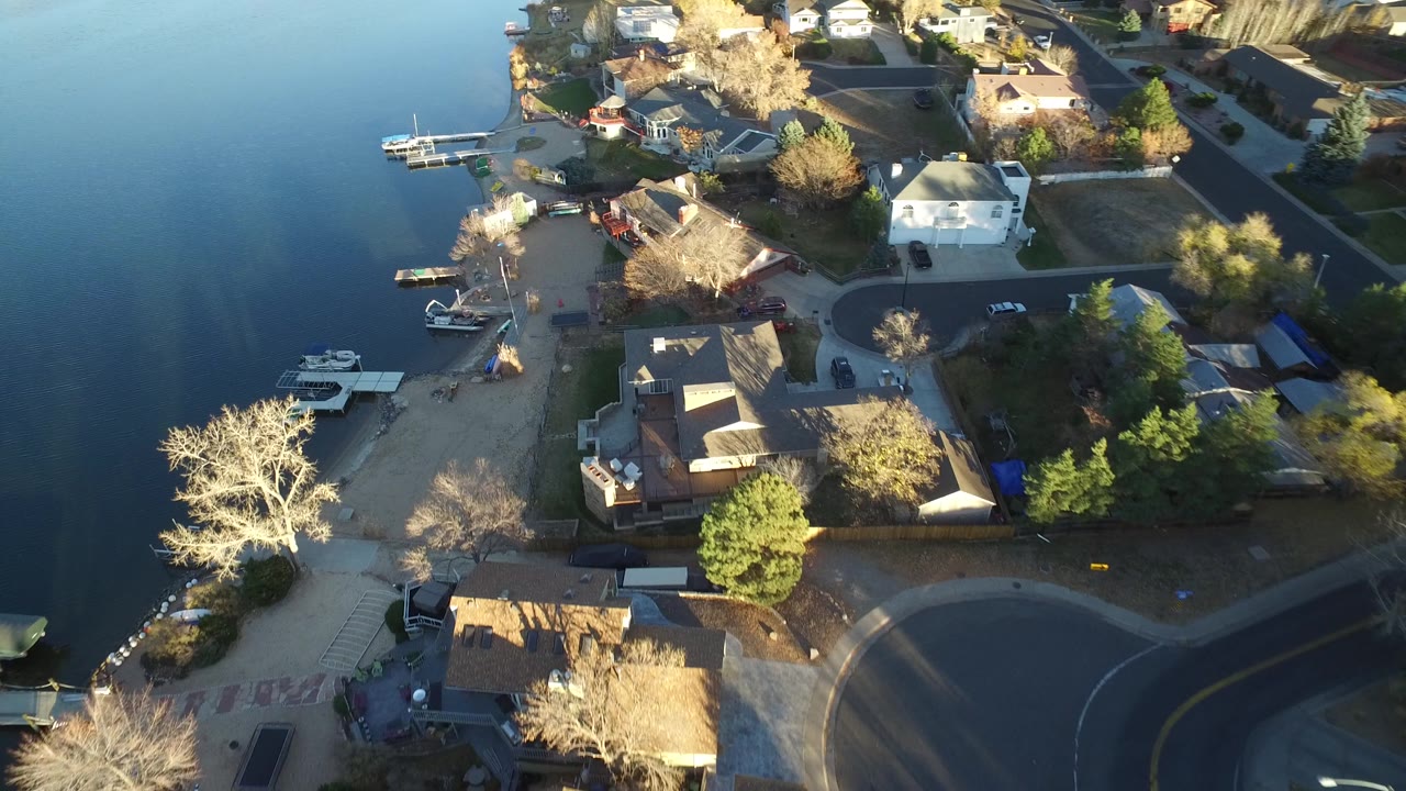 A second aerial frame in Westminster, Colorado holds over the shoreline, with blue lake water, small boats, docks, residential roofs, trees, and no visible people.
