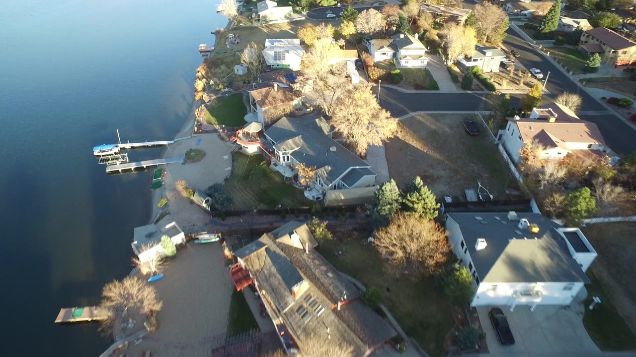 Aerial view of lakeside houses, docks, boats, streets, and bare trees.