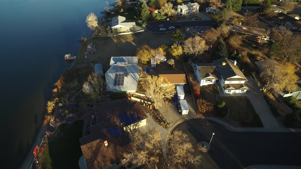 Oblique aerial frame over Westminster, Colorado homes beside calm water, with docks, parked cars, leafless and yellow trees, and no visible people.