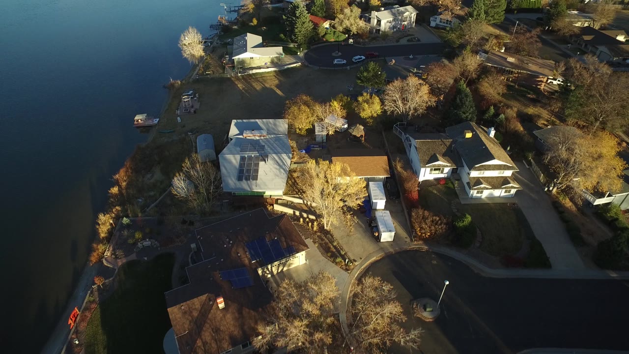 Aerial view in Westminster, Colorado with water on the left, homes and yards below, a rounded street area near the top, parked cars, small boats, and no visible people.