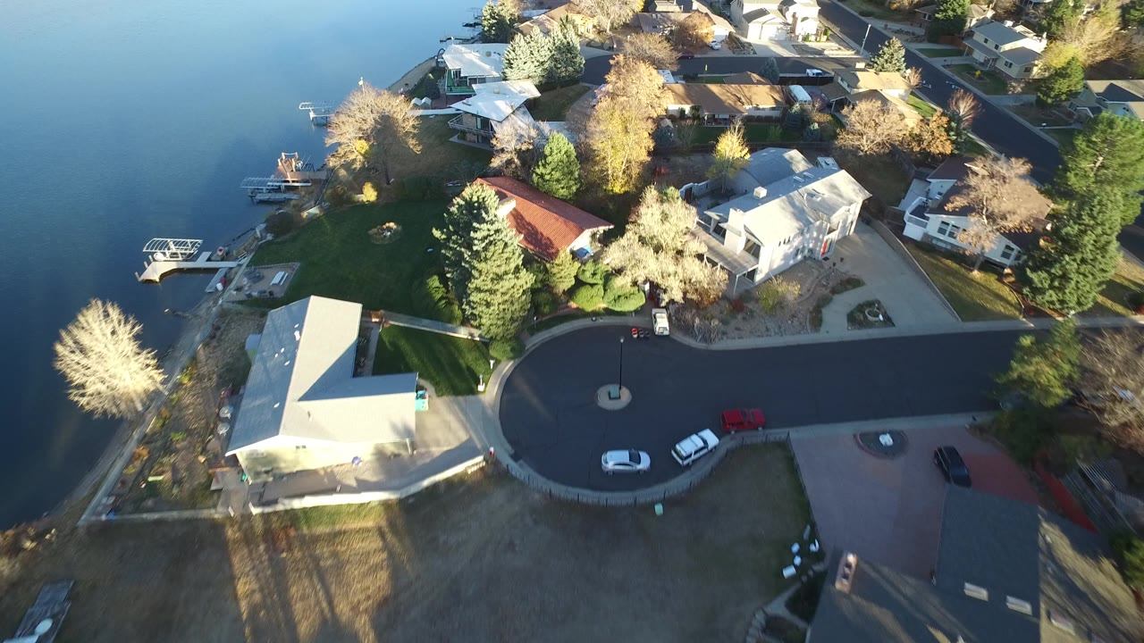 Lakefront subdivision viewed from above with docks, homes, trees, and streets.