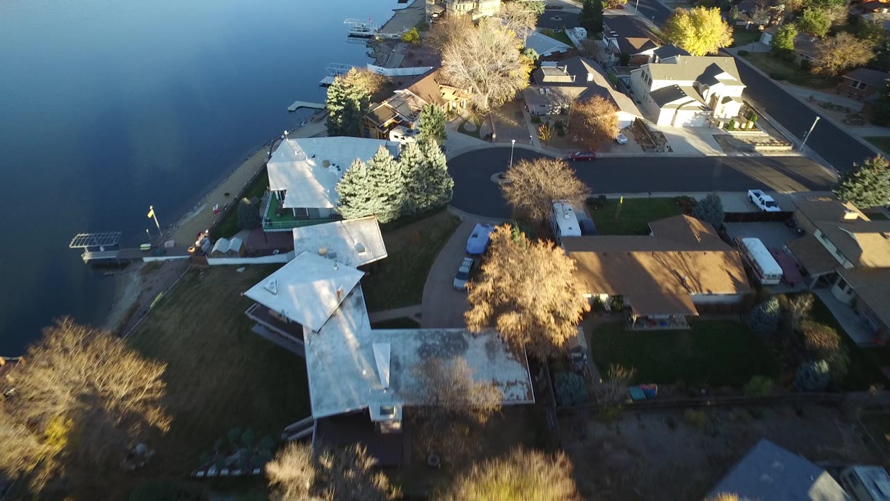 Aerial angle over a lakeside neighborhood with docks, houses, and a curved road.