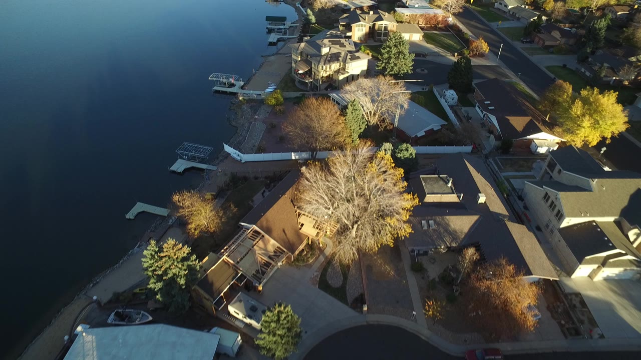 Aerial view of lakeside homes, docks, rooftops, and autumn trees.