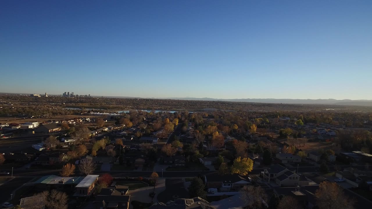 Wide aerial view over suburban houses and trees under a clear blue sky.