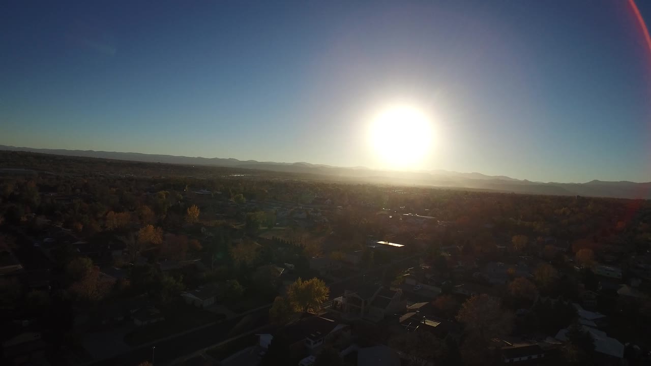 At 0:01, the sun sits near the center of the sky above Westminster, Colorado, with darkened trees and rooftops below and no visible people.