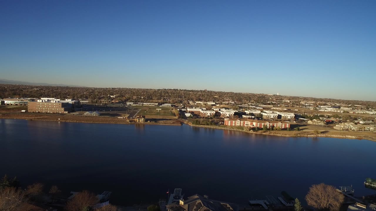 Wide aerial view over dark water toward shoreline homes and low buildings.