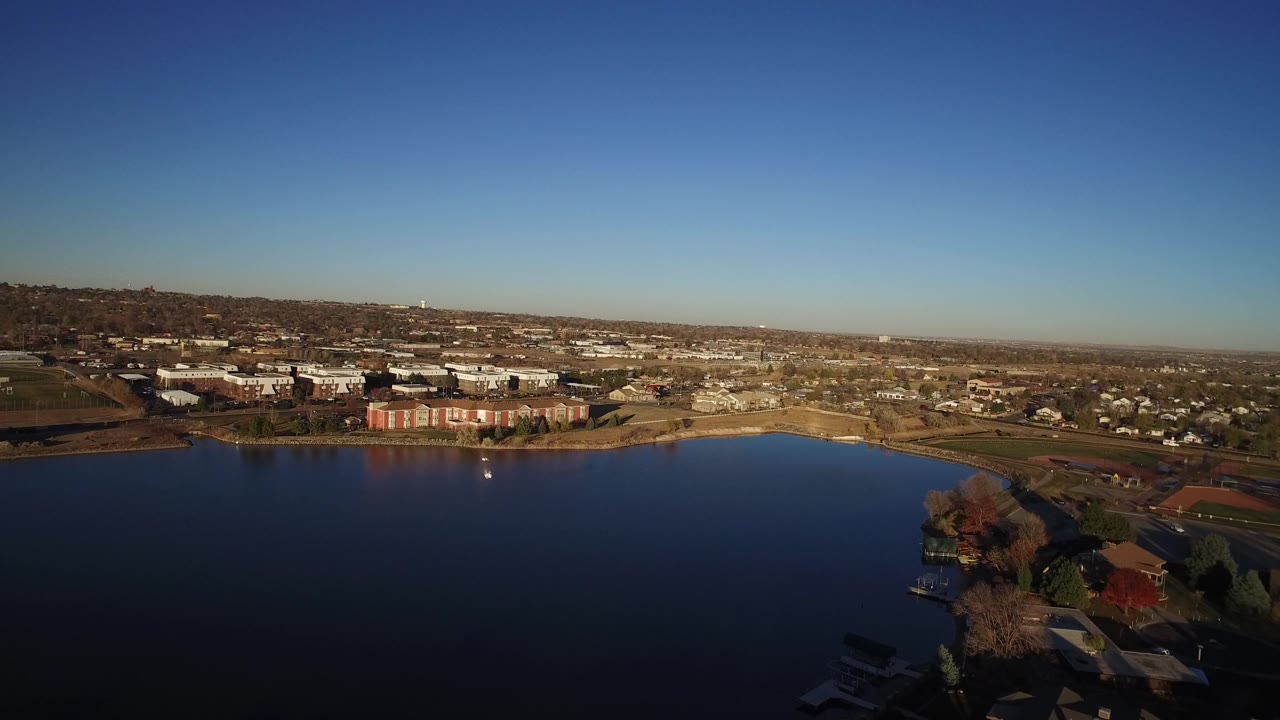 Aerial view of a lake beside suburban buildings under a clear sky.