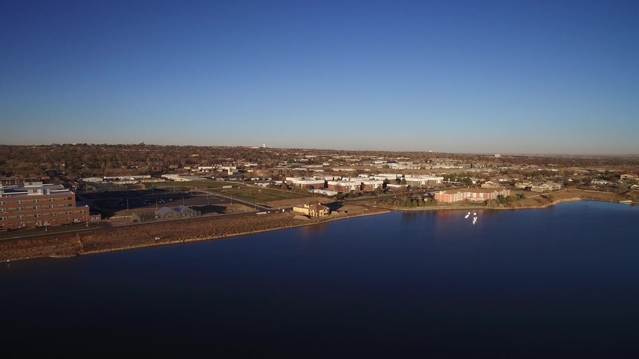 Aerial view across a dark blue lake toward low-rise buildings and suburban roads.