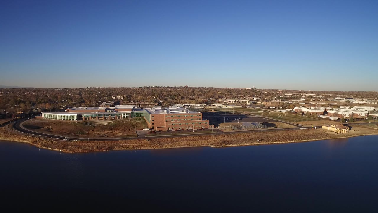 Aerial view over water toward suburban buildings and trees.