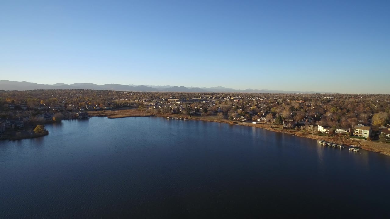 The second frame keeps the lake dominant in front while Westminster homes, scattered docks, leafless and autumn-toned trees, and distant mountains stretch across the background with no visible people.