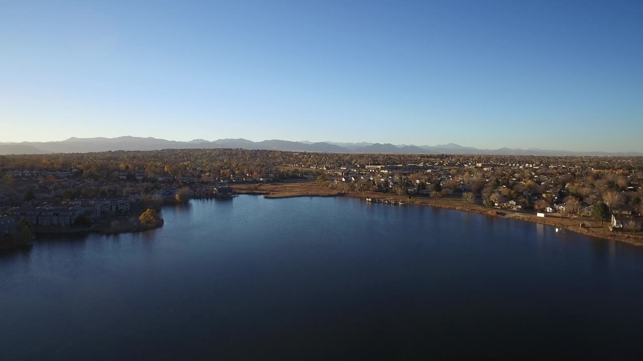 Wide aerial view of a large lake with neighborhoods and mountains beyond.