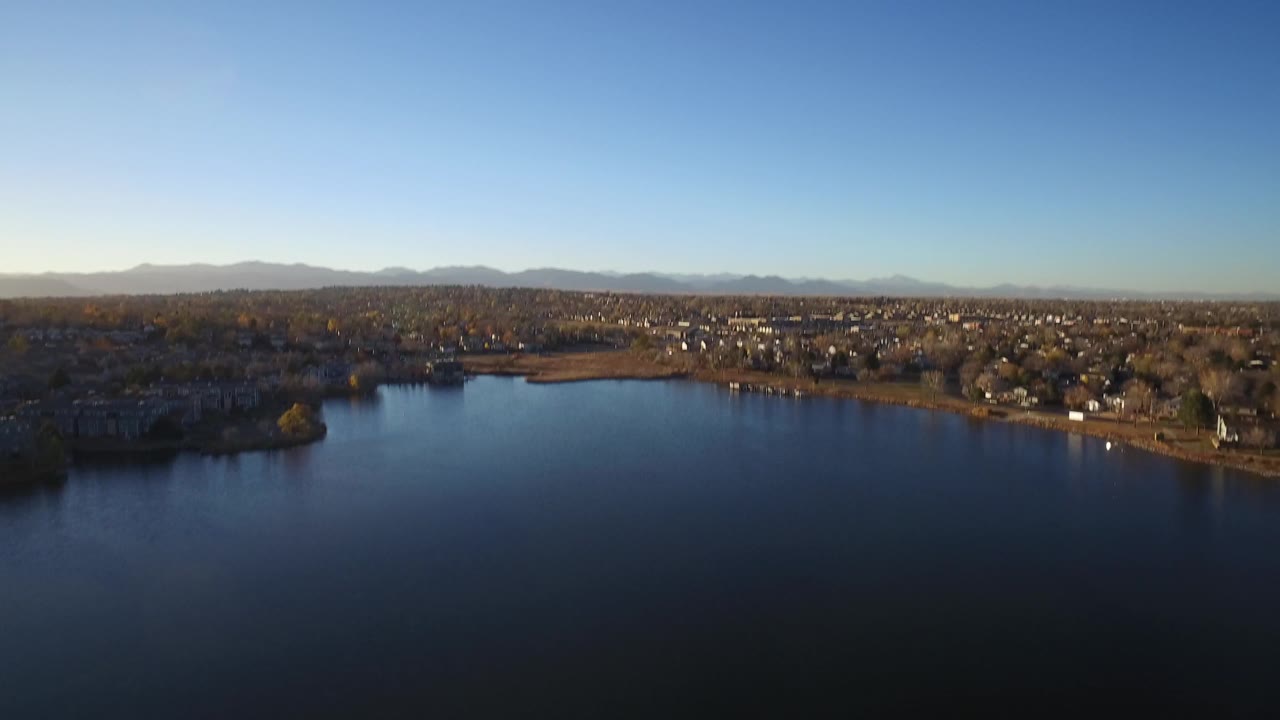 Aerial view of the Westminster lake looking across dark blue water toward shoreline homes, autumn-colored trees, distant mountains, and no visible people.