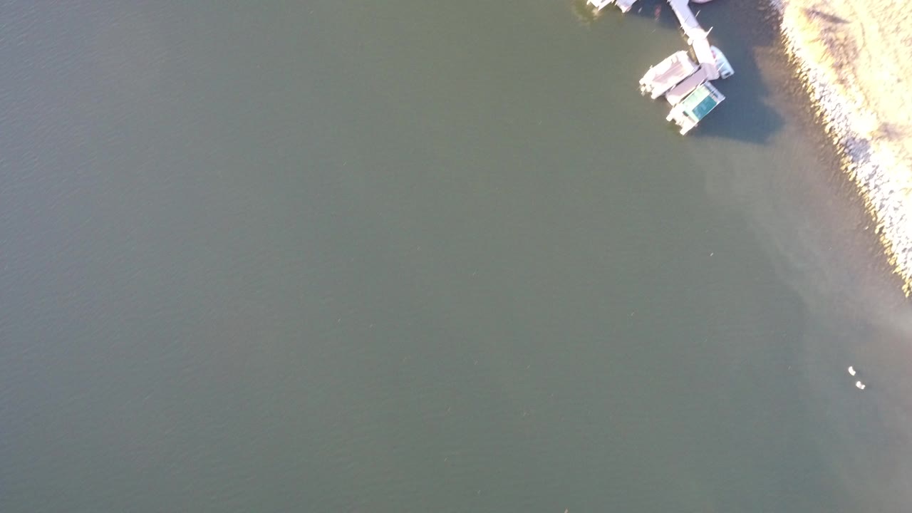 Top-down view of dark water beside a rocky shoreline and small dock structures.