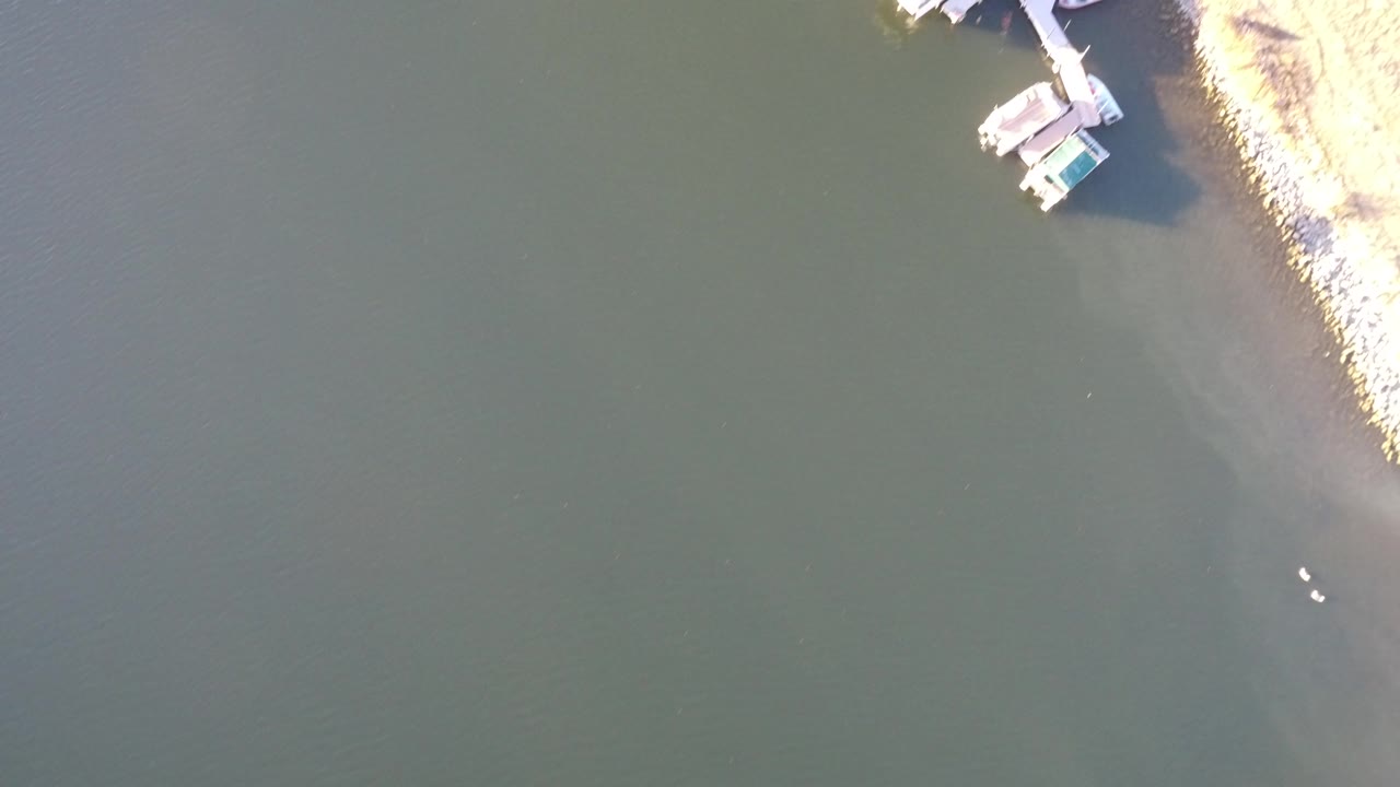 Top-down Westminster, Colorado aerial with mostly dark water, a pale rocky bank along the right side, small docks near the top edge, and no visible people.