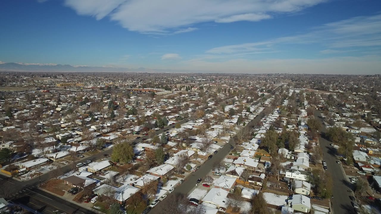 High aerial view over snow-dusted houses and streets under a blue sky.