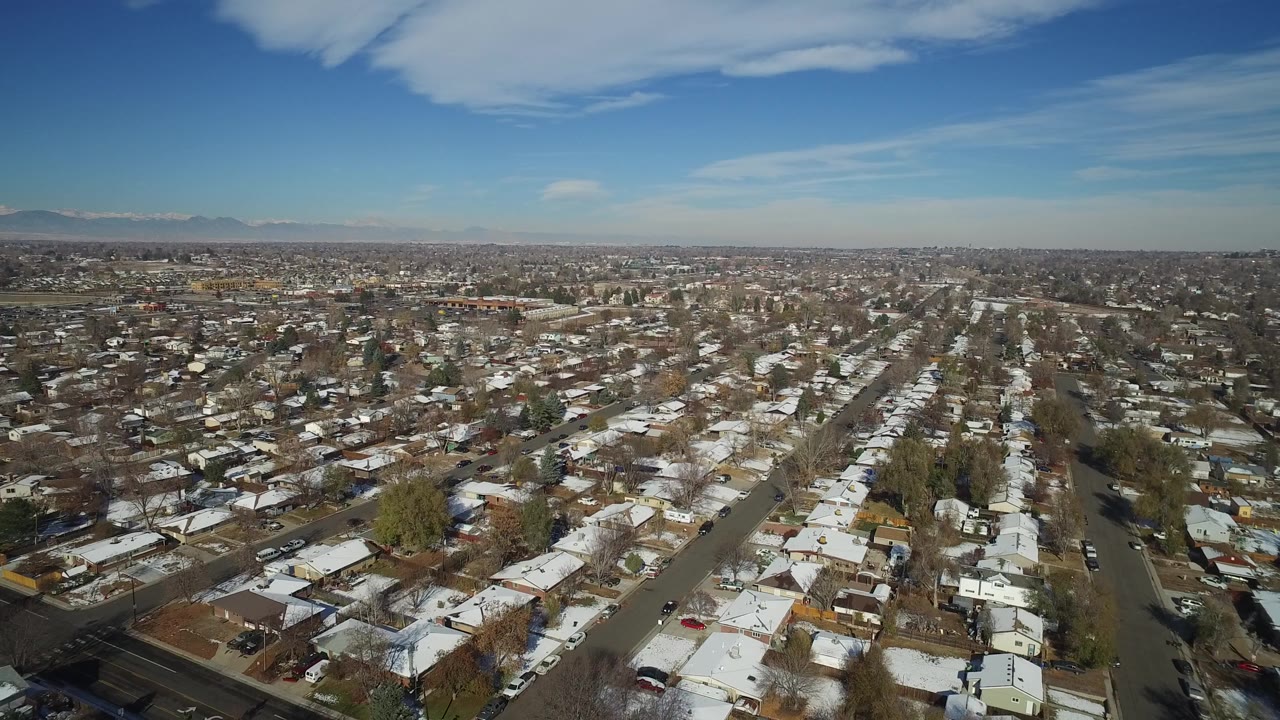 Second aerial frame over Hidden Lake, Colorado showing a gridded neighborhood, white roof patches, a broad blue sky, and no visible people.