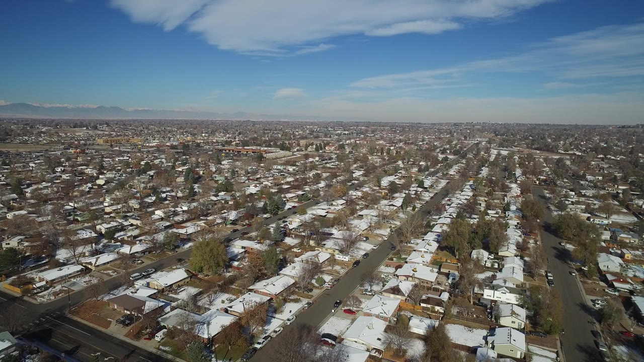 Mid-clip aerial frame over Hidden Lake, Colorado with rows of houses, a diagonal street, winter trees, distant mountains, and no visible people.