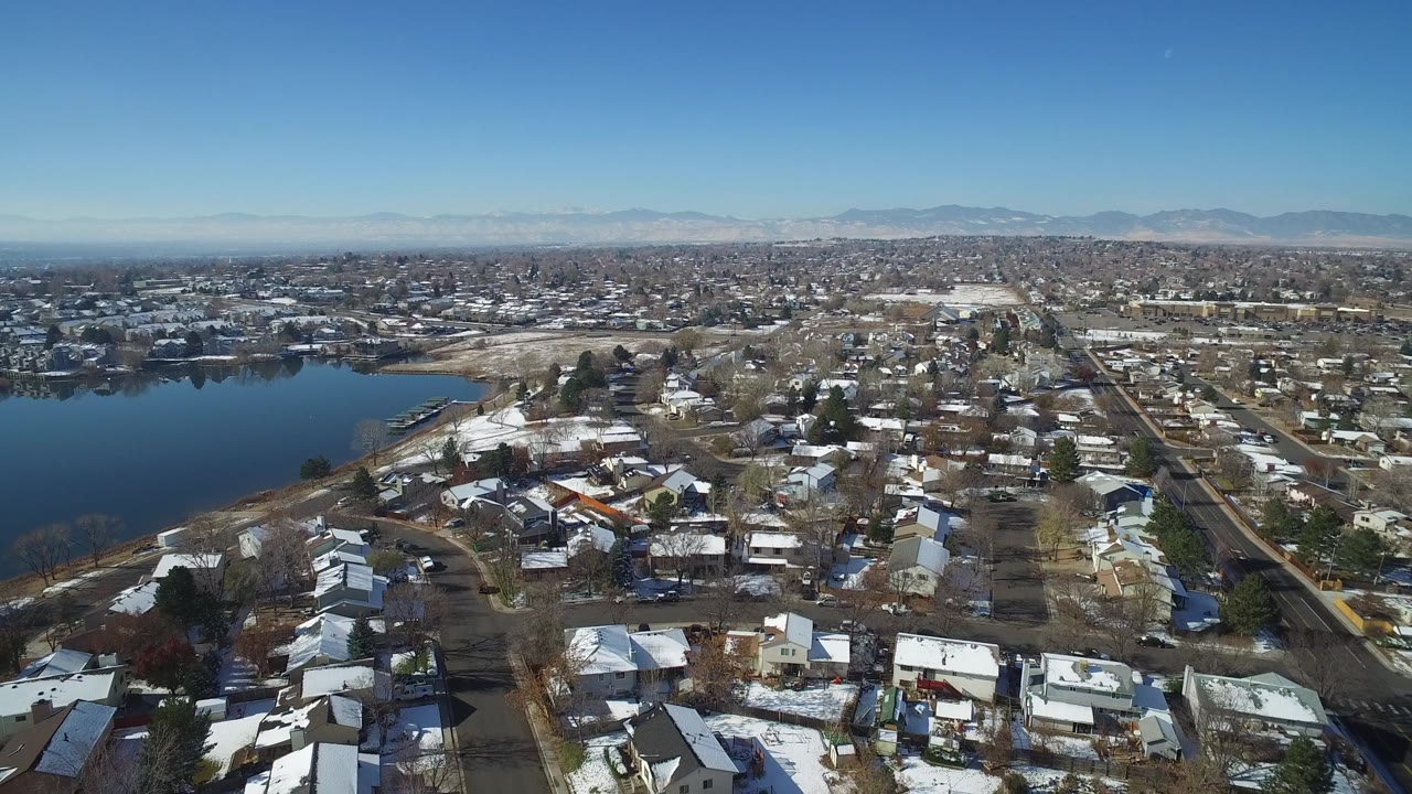 Aerial view of snowy homes beside a lake with mountains in the distance.