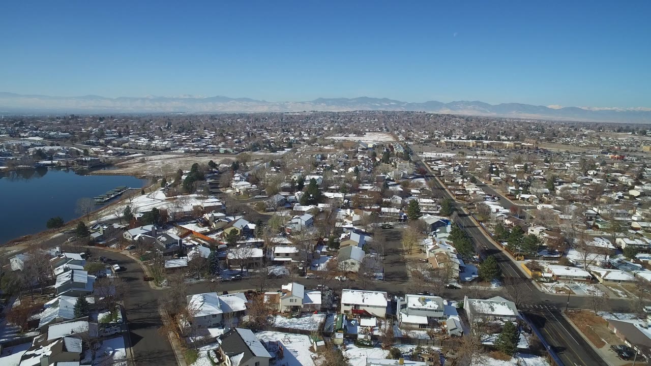 Second frame over Hidden Lake, Colorado with gridded residential streets, small homes, winter yards, the lake along the left edge, distant mountains, and no visible people.