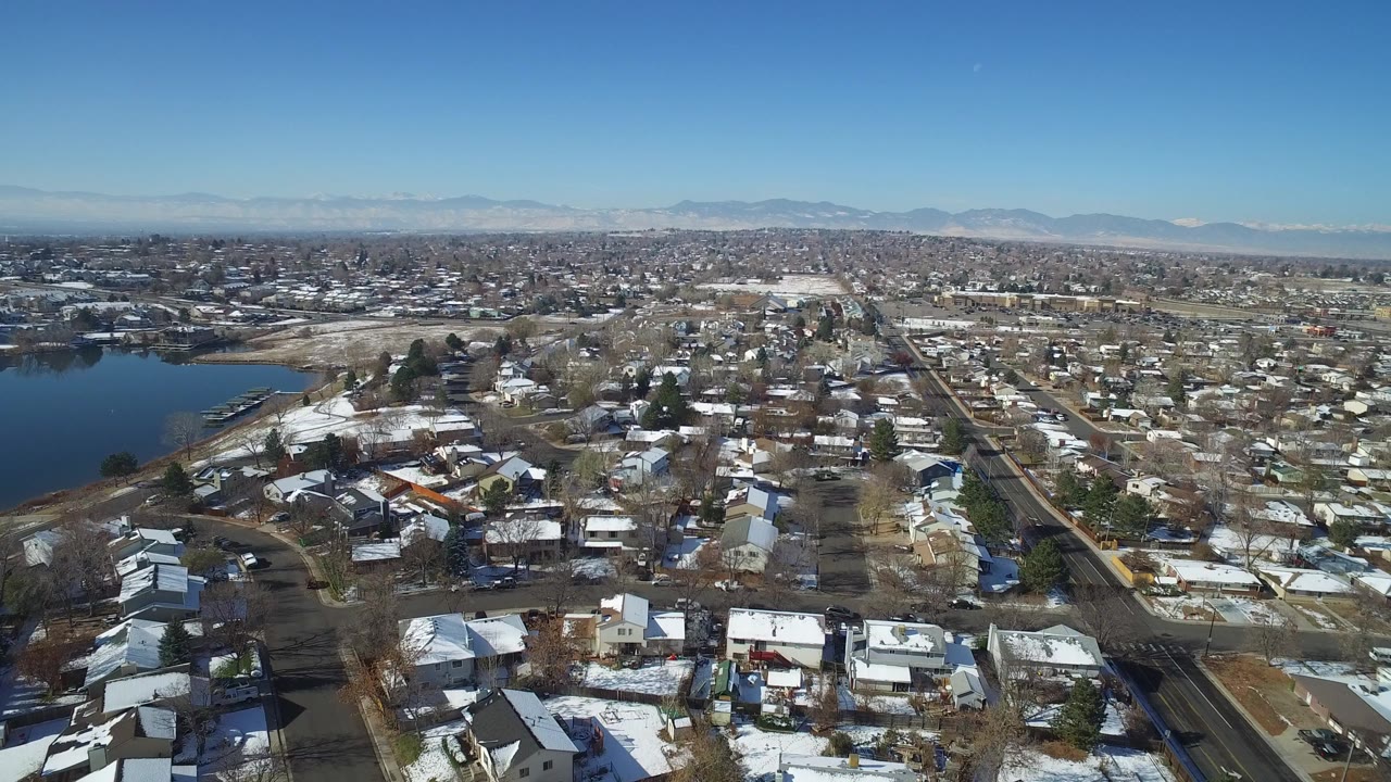 Aerial view of snow-dusted houses, roads, lake edge, and distant mountains.