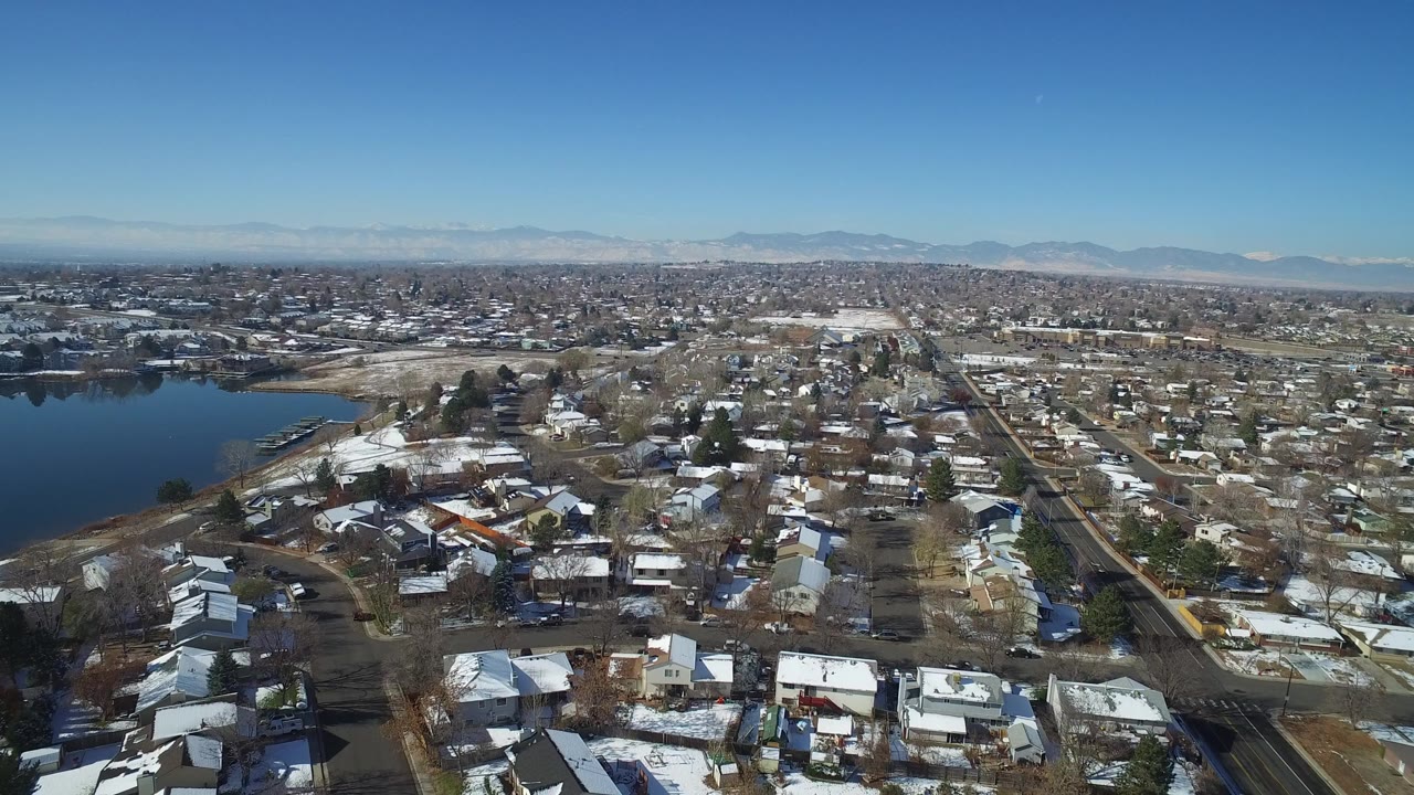 Wide aerial view over homes beside a lake under blue sky.