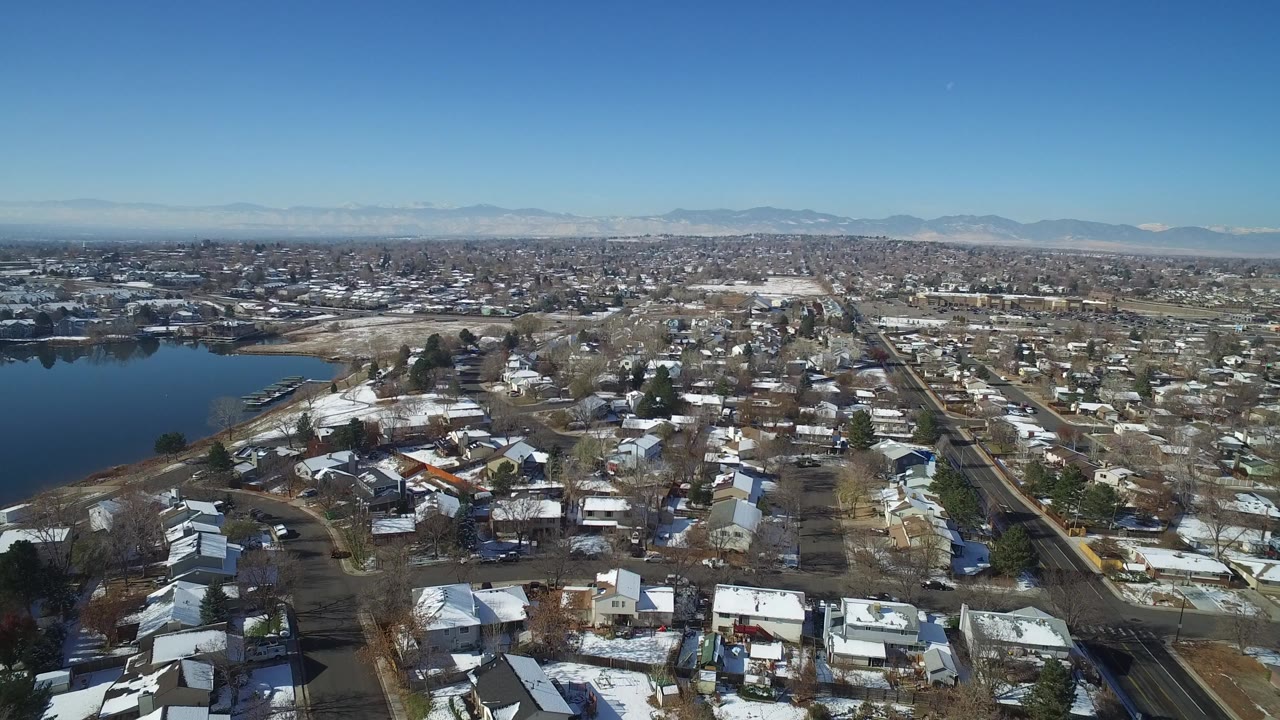 Opening aerial frame over Hidden Lake, Colorado, with a dark lake on the left, snow-dusted homes below, distant mountains, and no visible people.