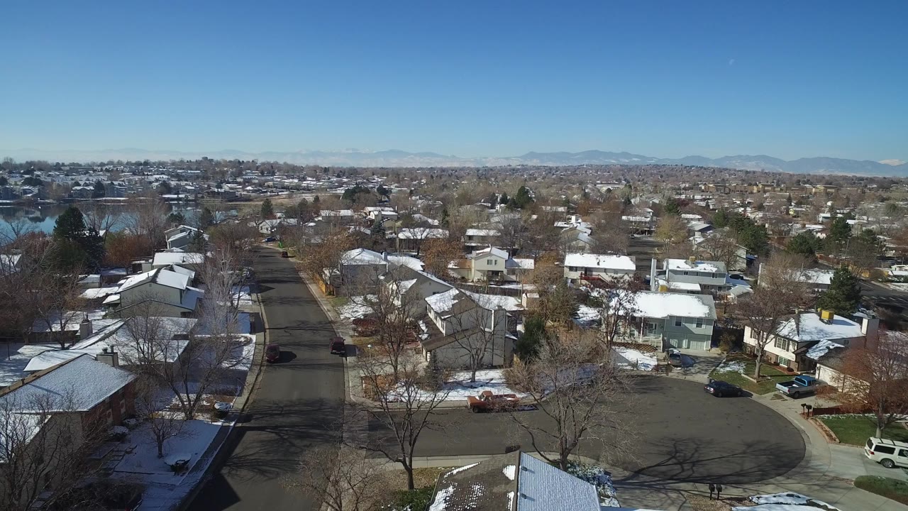 Aerial view over a quiet snowy suburban street and rooftops.