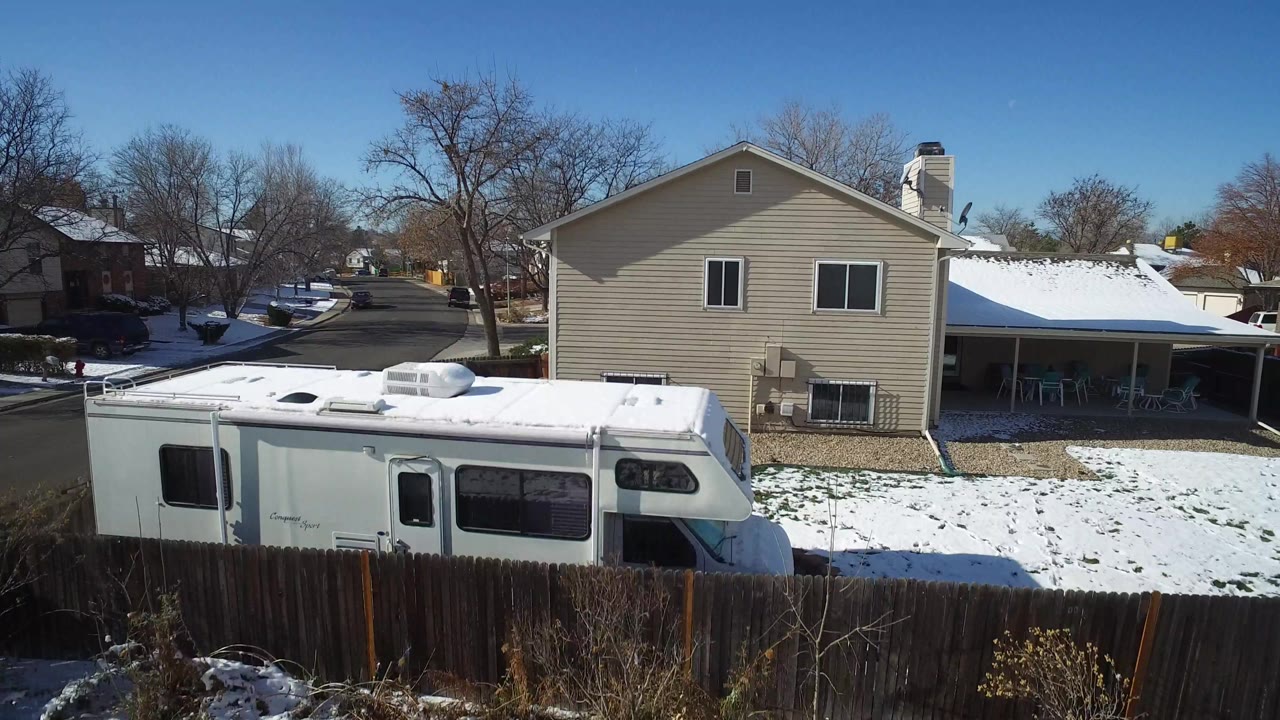 Aerial view of an RV beside a house with snowy lawns and a residential street.